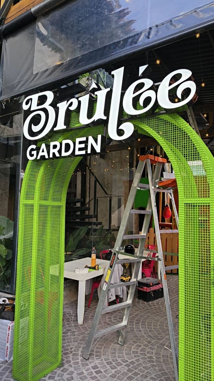 Letrero de Brûlée Garden sobre arco verde
